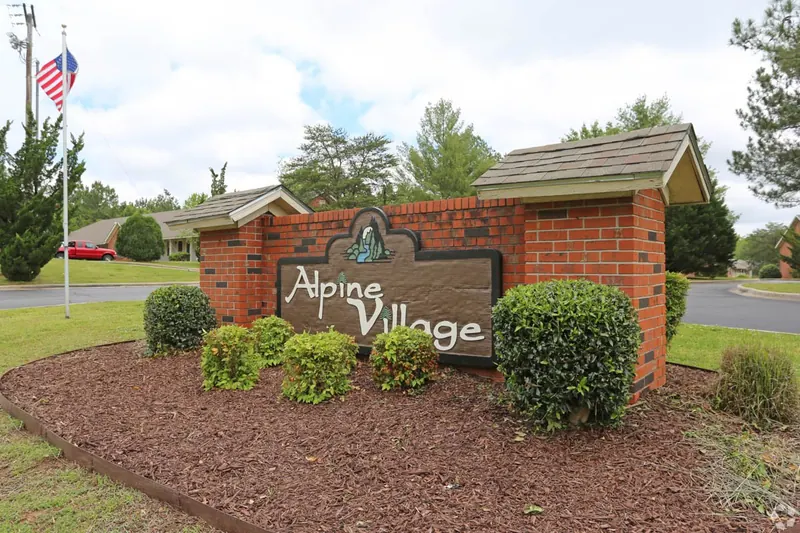 Alpine Village entrance sign with landscaping and an American flag